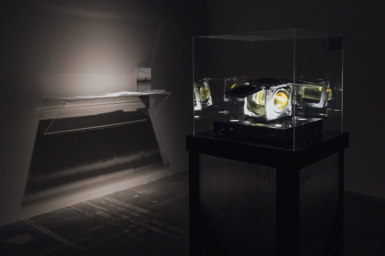 CubeSat model in a sealed vitrine, installation view