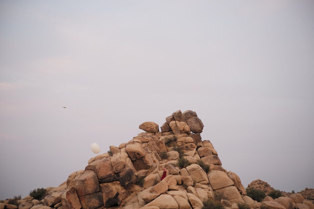 Small figure and white balloon on a granite boulder ridge in Joshua Tree National Park