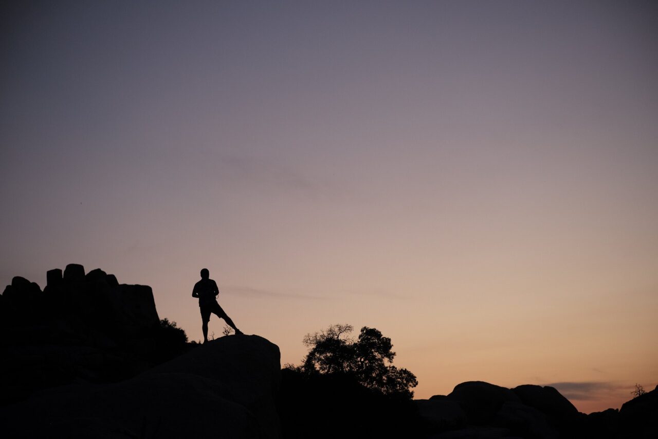 Silhouette of a person on a boulder ridge at dusk in Joshua Tree National Park