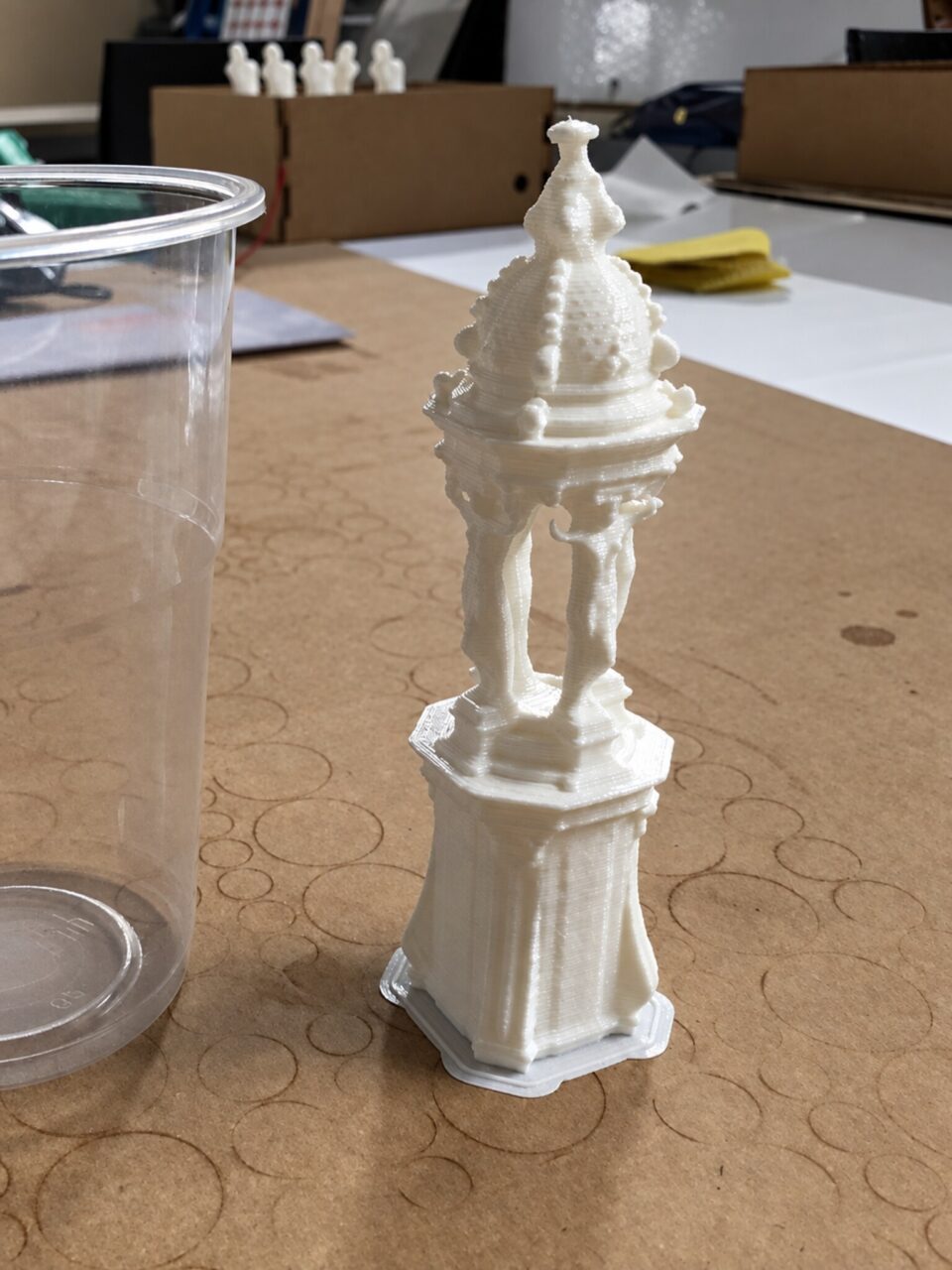 Small white printed model of an ornate monument or fountain standing on a cardboard work surface.