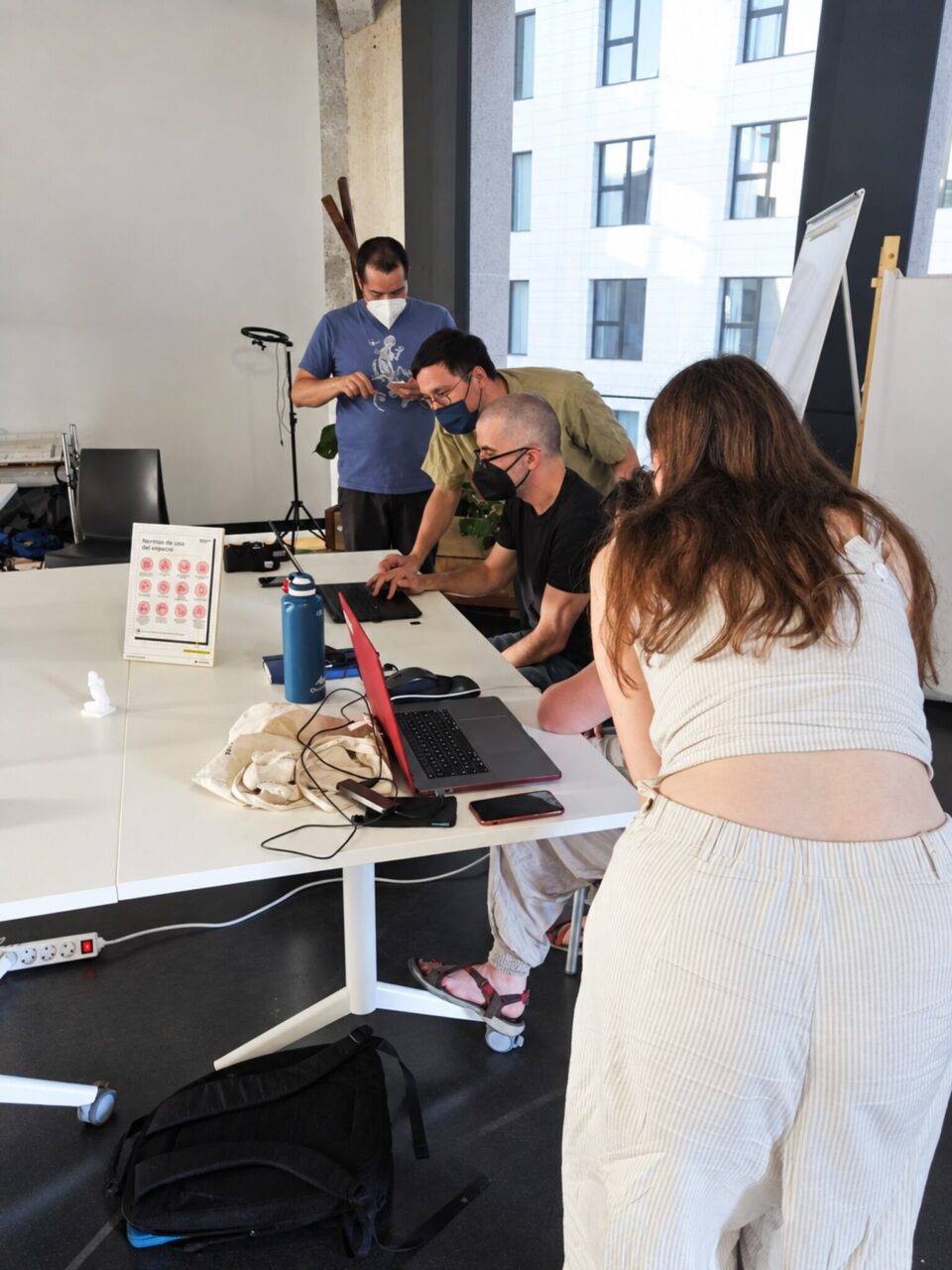Participants gathered around a white table with laptops and a tripod, one woman leaning over to look at a screen.