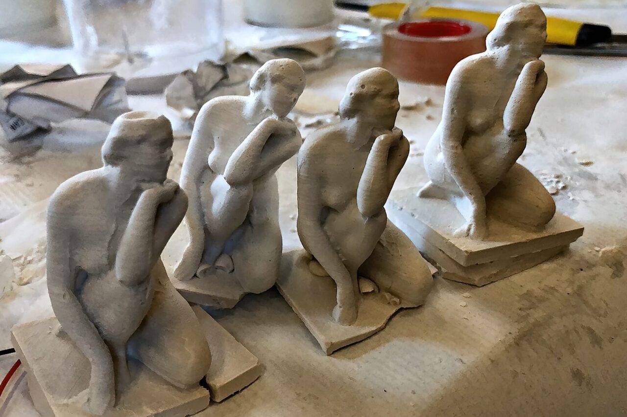 Four white plaster casts of a kneeling figure in a row on a dusty workbench.